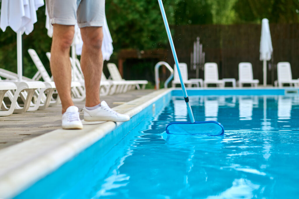 A homeowner cleaning their swimming pool with a net tool